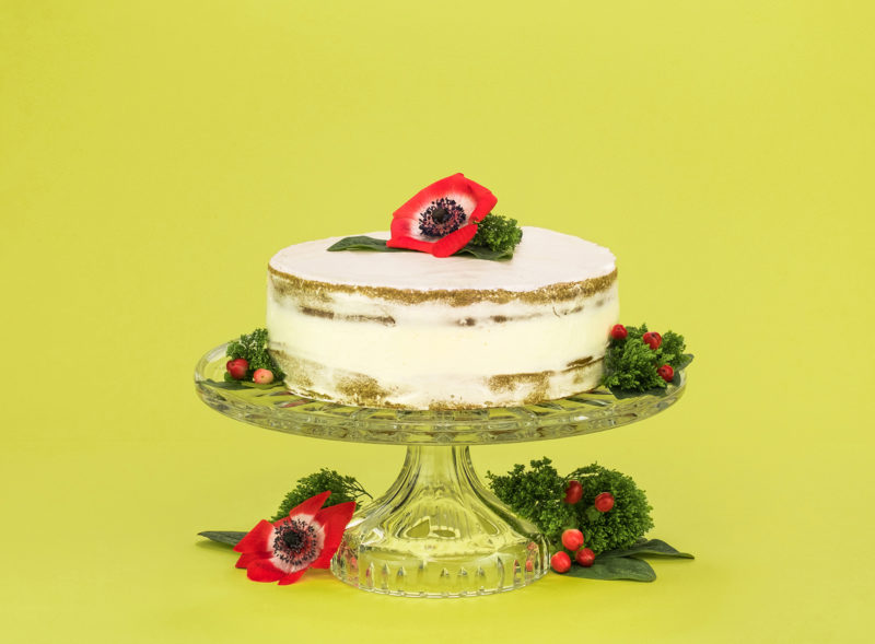 A photograph of a cake on a stand with flowers